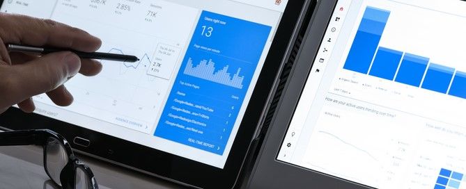 Há duas telas que apresentam gráficos e dados. Do lado esquerdo da imagem uma mão mexe com uma caneta smart em uma das telas