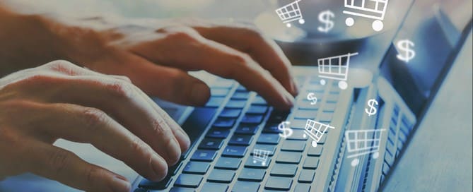 Duas mãos digitando em um teclado de notebook com representações de ícones de carrinho de compras e cifrões ao redor