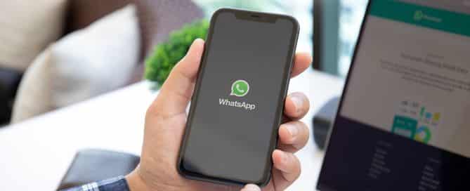 uma mão segura um celular com a tela apagada e o logo do whatsapp
