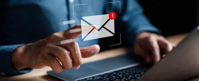 A imagem mostra a mão de um homem e o teclado de notebook em foco. Em primeiro plano tem a ilustração de uma caixa de mensagens do e-mail com uma notificação.