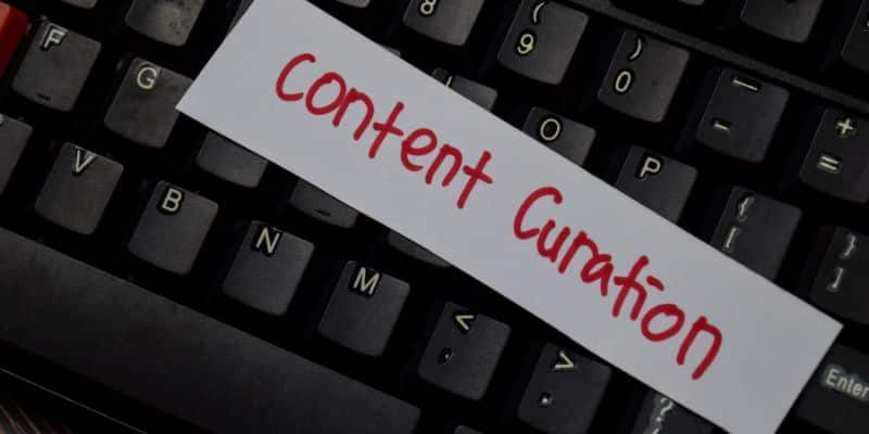 A imagem mostra um teclado de computador com um papel escrito "content curation", a expressão em inglês de curadoria de conteúdo