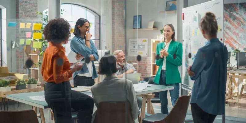 A imagem mostra uma equipe de marketing tendo uma reunião dentro de uma sala de vidro