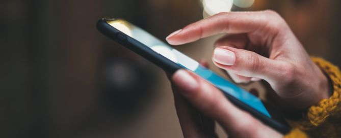 A imagem mostra um celular e uma mão feminina mexendo nele.