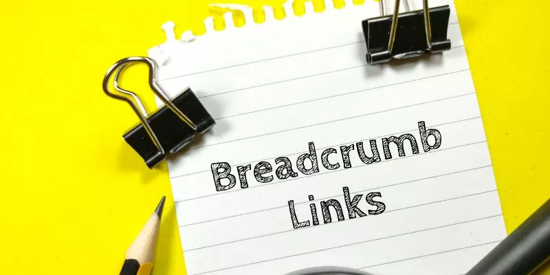 Imagem de uma folha de papel escrita "Breadcrumb Links". Há dois pregadores ao redor das palavras e a ponta de um lápis na parte inferior esquerda da imagem.