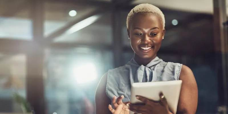 Mulher preta de cabelo branco e curto segurando um tablet e sorrindo para ele.