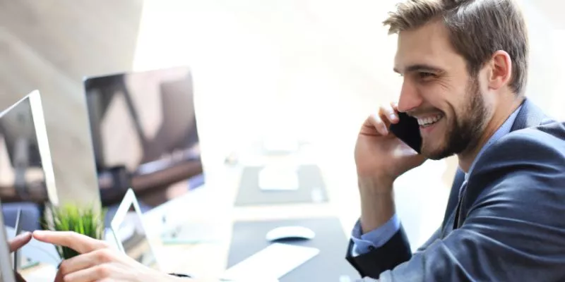 Homem ao telefone em frente a um computador. Ele está sorrindo, simulando uma conversa positiva com um cliente, ou seja, o Pitch de Vendas está indo como planejado