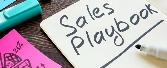 Papéis espalhados em cima de uma mesa. Em um deles está escrito "Sales Playbook", que significa Playbook de Vendas em inglês