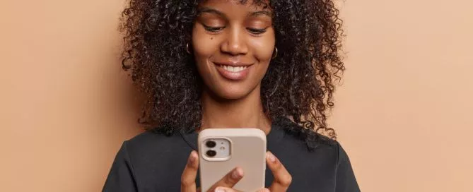 Mulher sorrindo enquanto mexe no celular. Representa a experiência do usuário em um site Mobile Friendly