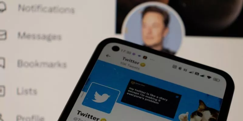 Perfil oficial do Twitter em um smartphone com o de Elon Musk desfocado no fundo.