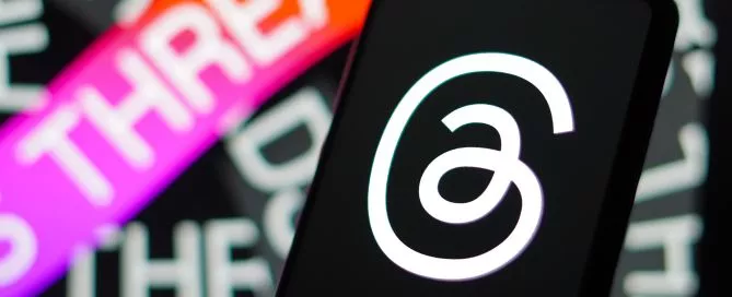 Imagem mostra um celular com o logo do Threads na leta. Loho atrás, está o nome do aplicativo.