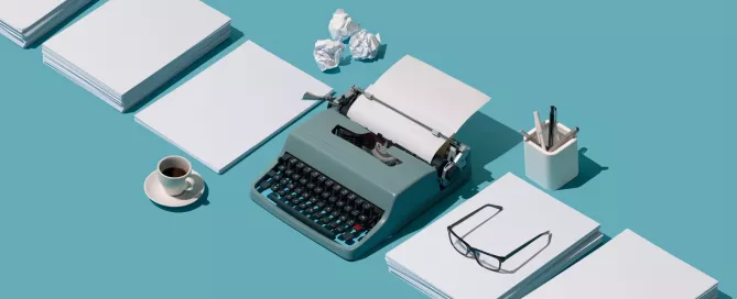 A foto possui um fundo azul que simula uma mesa onde, no meio, está uma maquina de escrever também azul e ao lado direito e esquerdo estão pilhas de papéis. E uma das pilhas tem um óculos.