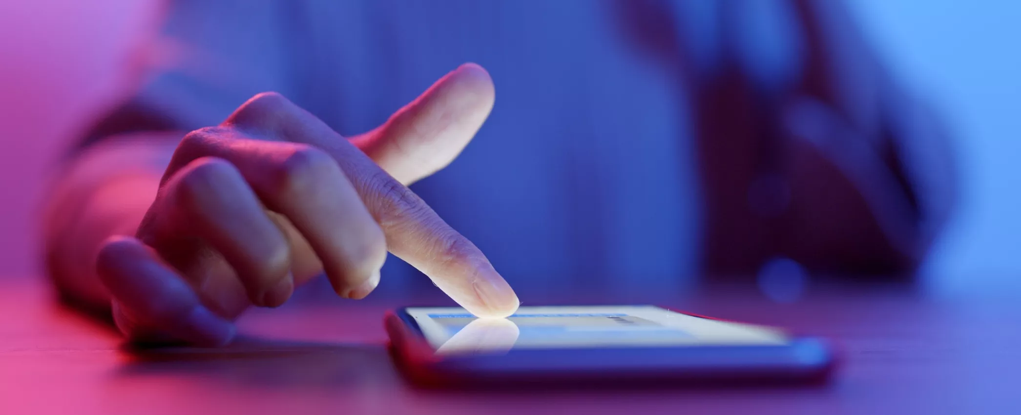 A foto mostra a mão de uma pessoa tocando na tela de um celular.