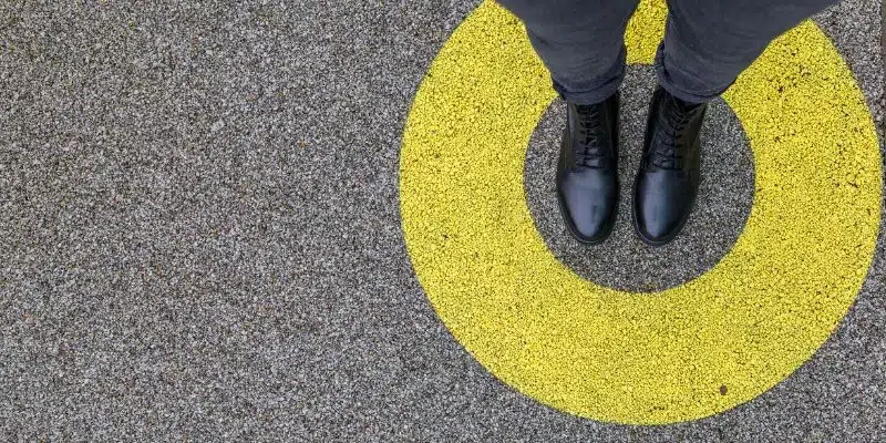 A imagem mostra o chão de uma rua com um desenho de circulo amarelo, no centro desse circulo tem um homem