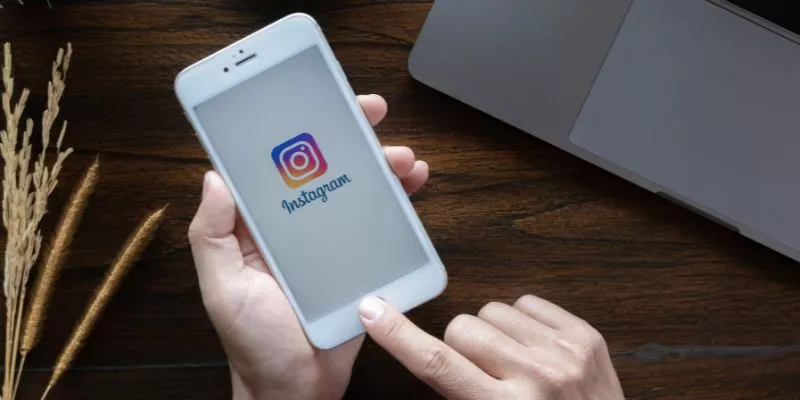 A imagem mostra uma pessoa segurando um celular, na tela do aparelho está o logo do Instagram.