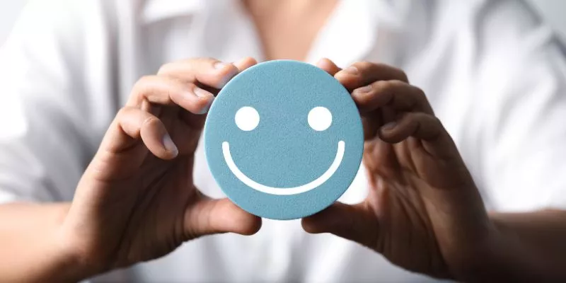 A imagem mostra uma pessoa segurando um círculo com uma carinha feliz desenhada.